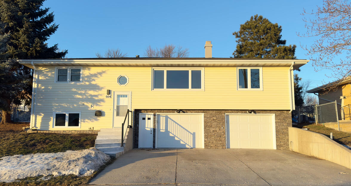 Exterior residential house painting in Mandan, ND, by Will Contracting, showing freshly painted light yellow siding, white trim, and a grey foundation on a split-level home.