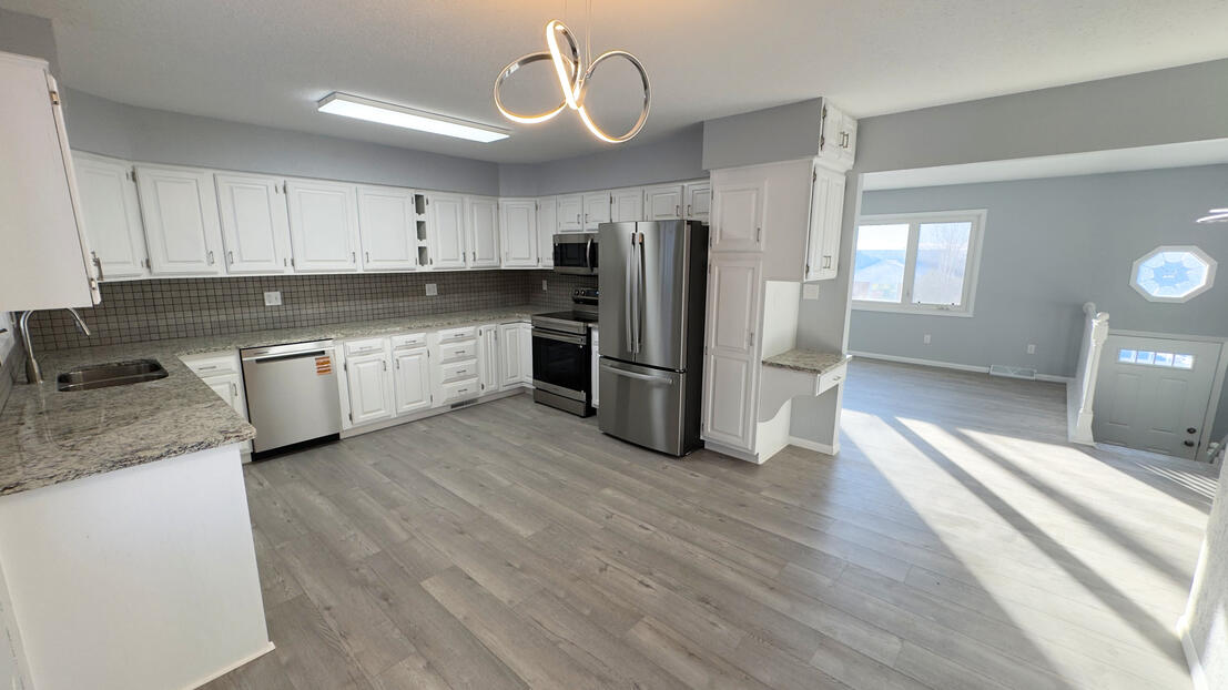 Renovated open-concept kitchen with Will Contracting’s signature white cabinet finish, dynamic stone backsplash, and wood-look LVP flooring