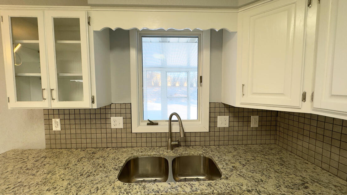 Symmetrical view of a renovated kitchen sink area with crisp white painted cabinets, modern mosaic backsplash, and quartz countertops.