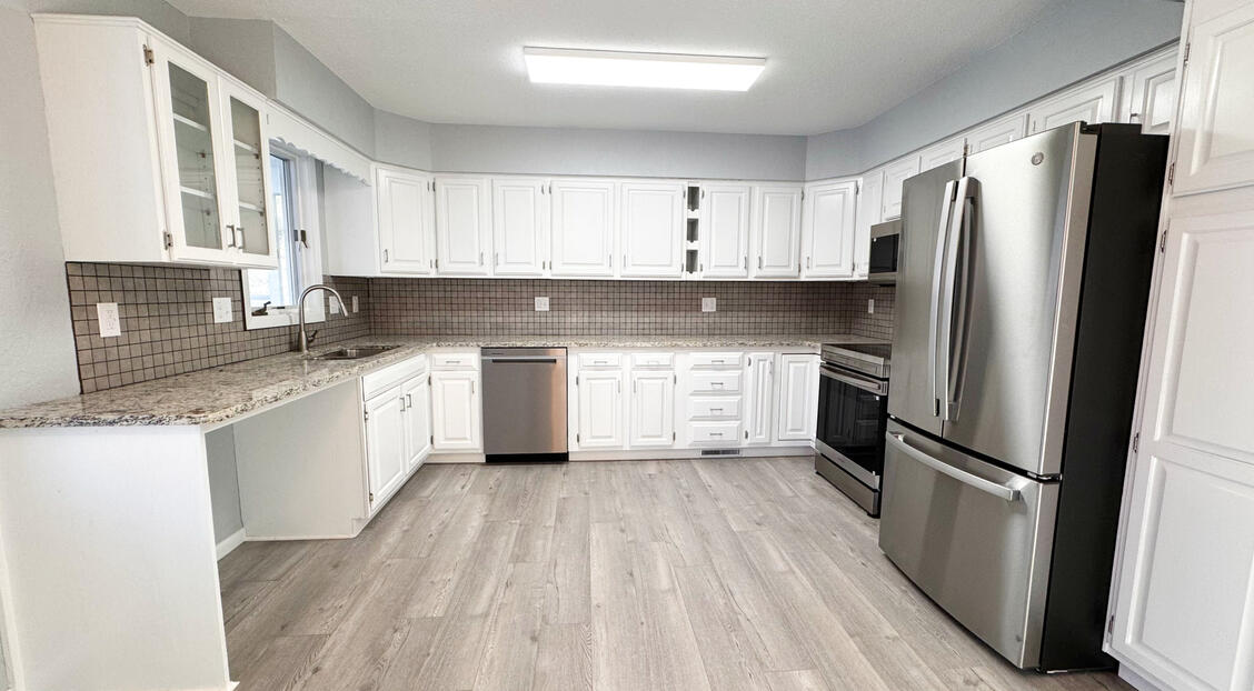 Total kitchen remodel showing new white shaker cabinets, light wood-look flooring, stone backsplash, and stainless steel appliances